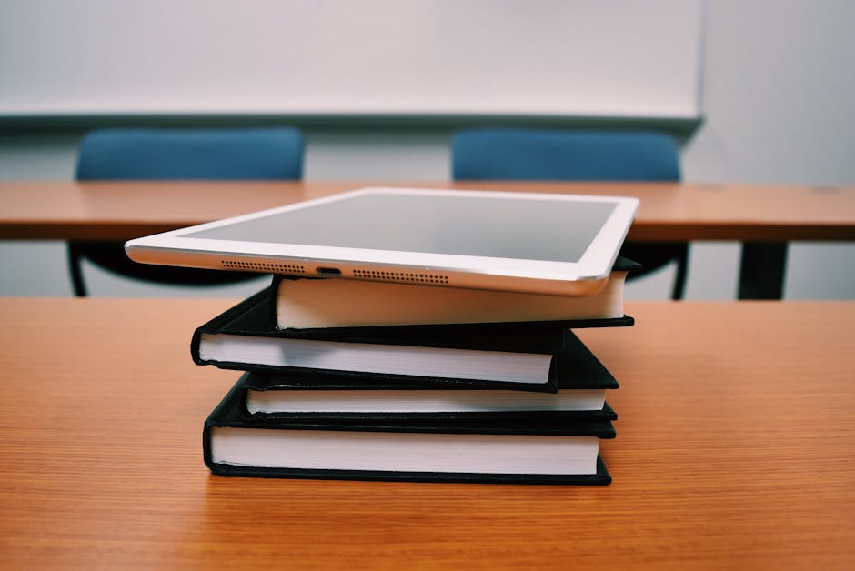 A tablet rests on top of a stack of books in an empty classroom, illustrating modern education